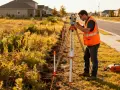 Geodeta w kamizelce odblaskowej pracuje przy tachimetrze. Określa, ile kosztuje podział działki na 4.