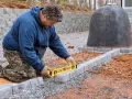 Budowniczy sprawdza poziom kostki brukowej, by zapewnić idealny spadek na kostce brukowej. Obok stoi nietypowy, czarny obiekt.