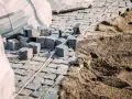 Kupa kostki brukowej i piasku, gotowe do ułożenia. Widać worki z materiałem i przygotowany podkład, czyli ile podsypki pod kostkę potrzeba.