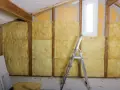 Prace nad izolacją ścian od wewnątrz przed wilgocią. Wełna mineralna wypełnia przestrzenie między drewnianymi belkami.