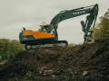 Pomarańczowo-czarna koparka Volvo EC220DL pracuje na budowie. Operator koparki gąsienicowej zarabia dobrze, wykonując ciężką pracę.