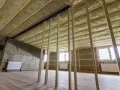 Ocieplenie stropu betonowego wełną mineralną. Widać drewnianą konstrukcję, okna i grzejniki.