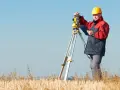 Geodeta w żółtym kasku pracuje z tachimetrem na polu. Zastanawiasz się, ile bierze geodeta za podział działki?