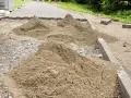 Kopce piasku czekają na ułożenie kostki brukowej. Trudno oszacować, ile piasku na m2 kostki, ale materiału jest sporo.