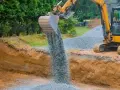 Koparka wysypuje tłuczeń do wykopu, tworząc fundament pod przyszłą drogę.