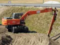 Pomarańczowa koparka Hitachi Zaxis 160W pracuje na budowie. Operator z uprawnieniami na minikoparkę wykonuje prace ziemne.