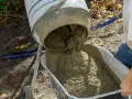 Betoniarka wylewa świeży beton do taczki. Właściwa ilość cementu na 1 m3 betonu jest kluczowa dla jego wytrzymałości.