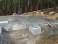 Solidna płyta fundamentowa, gotowa na budowę domu. Wokół las i drewniany płot.