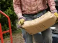 Mężczyzna w rękawicach niesie worek cementu, zastanawiając się, ile cementu do piasku potrzeba do zaprawy.
