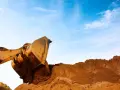 Żółta koparka z wielką łyżką nabiera ziemi na tle błękitnego nieba. Zastanawiasz się, ile pali koparka na godzinę?