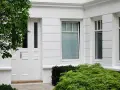 Boniowanie elewacji domu podkreśla jego klasyczny charakter. Białe drzwi i okna, otoczone zielenią, tworzą elegancką całość.
