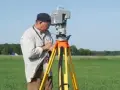Geodeta precyzyjnie ustala granice działki, używając nowoczesnego sprzętu pomiarowego na tle zielonego pola.