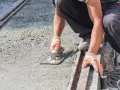 Pracownik w rękawicach wygładza świeży beton kielnią. To kluczowy etap, jak zrobić suchy beton, by był równy i trwały.