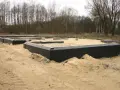Fundament domu w piasku, z czarną izolacją przeciwwilgociową wokół.