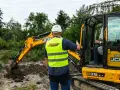 Instruktor nadzoruje kurs koparki klasa 3. Operator w kabinie, drugi pracownik w kamizelce odblaskowej.
