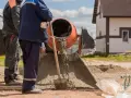 Dwóch budowlańców miesza beton. Zastanawiamy się, ile łopat żwiru na worek cementu, by uzyskać idealną konsystencję.