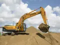 Koparka Hyundai z łyżką pełną piasku nad zwałami. Zastanawiasz się, ile kosztuje tona piasku?