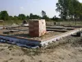 Budowa domu w toku. Widać zarys fundamentów, zbrojenie i ułożoną cegłę. Na środku placu budowy stoi paleta cegieł.