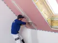 Fachowiec wykonuje gipsowanie ścian z płyty gipsowo-kartonowej, nakładając masę szpachlową na połączenie płyt.