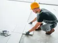 Fachowiec układa płytki na balkonie. Dowiedz się, ile kosztuje położenie płytek na balkonie i jakie materiały są potrzebne.