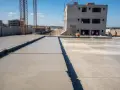 Plac budowy z nowo wylanym betonem, budynkiem w tle i dźwigami. Zastanawiasz się, ile betonu z worka cementu?