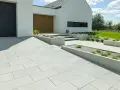 Nowoczesne wzory kostki brukowej przed domem tworzą schludny podjazd i ścieżki, otoczone geometrycznymi rabatami.