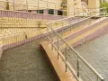 Podjazd dla niepełnosprawnych z poręczą, wykonany z cegły i płyt chodnikowych.