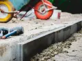 Dwa gumowe młotki leżą obok świeżo ułożonych krawężników. W tle widać taczkę, sugerującą prace budowlane i potrzebę odpowiedniej podsypki pod krawężniki proporcje.