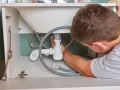 Hydraulik naprawia syfon pod zlewem. Zastanawiasz się, ile kosztuje hydraulik?