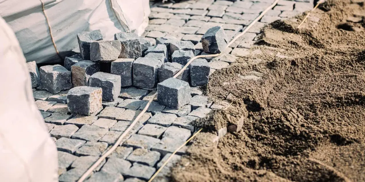 Kupa kostki brukowej i piasku, gotowe do ułożenia. Widać worki z materiałem i przygotowany podkład, czyli ile podsypki pod kostkę potrzeba.