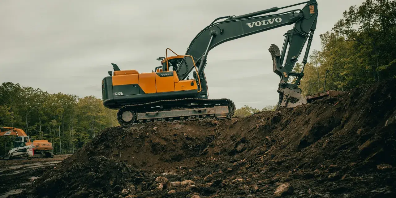 Pomarańczowo-czarna koparka Volvo EC220DL pracuje na budowie. Operator koparki gąsienicowej zarabia dobrze, wykonując ciężką pracę.