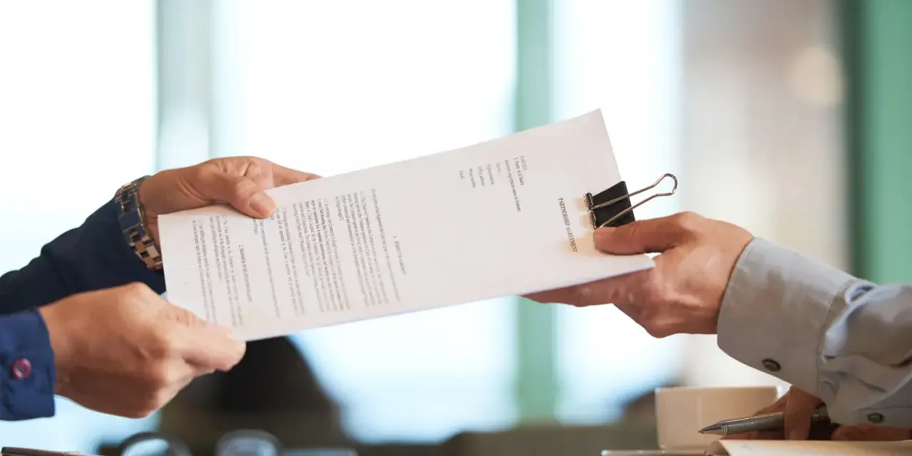 Dwie osoby przekazują sobie dokument "PARTNERSHIP AGREEMENT". To ważny moment, być może ustalanie co to dtr w umowie.
