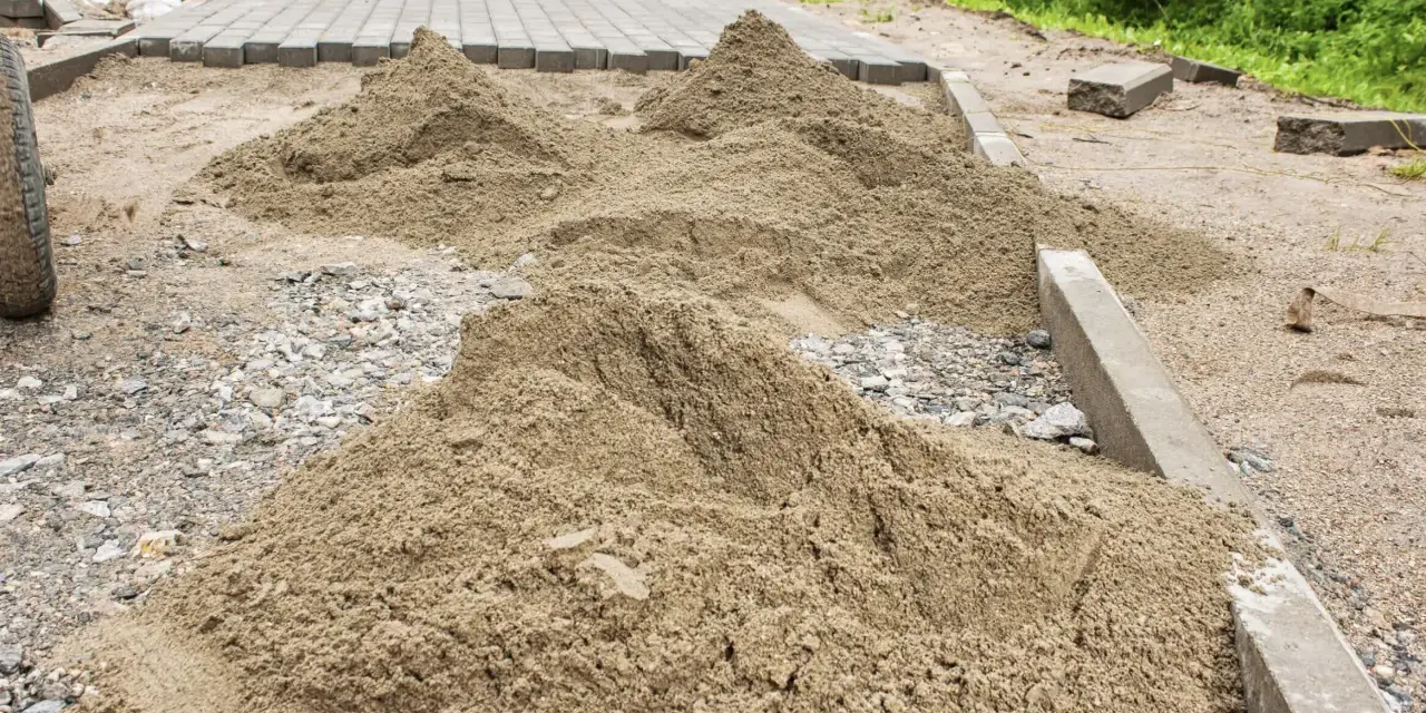 Kopce piasku czekają na ułożenie kostki brukowej. Trudno oszacować, ile piasku na m2 kostki, ale materiału jest sporo.