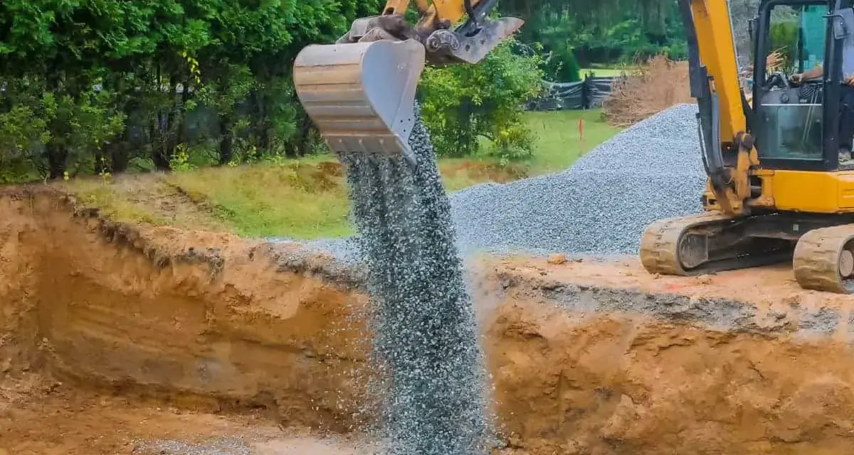 Koparka wysypuje tłuczeń do wykopu, tworząc fundament pod przyszłą drogę.