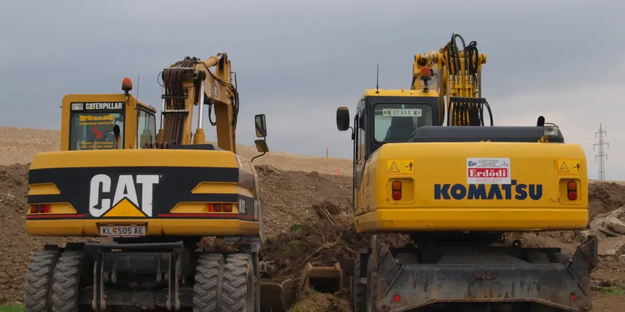Dwie żółte koparko-ładowarki, CAT i Komatsu, stoją na placu budowy. Czy koparko ładowarka musi być zarejestrowana?