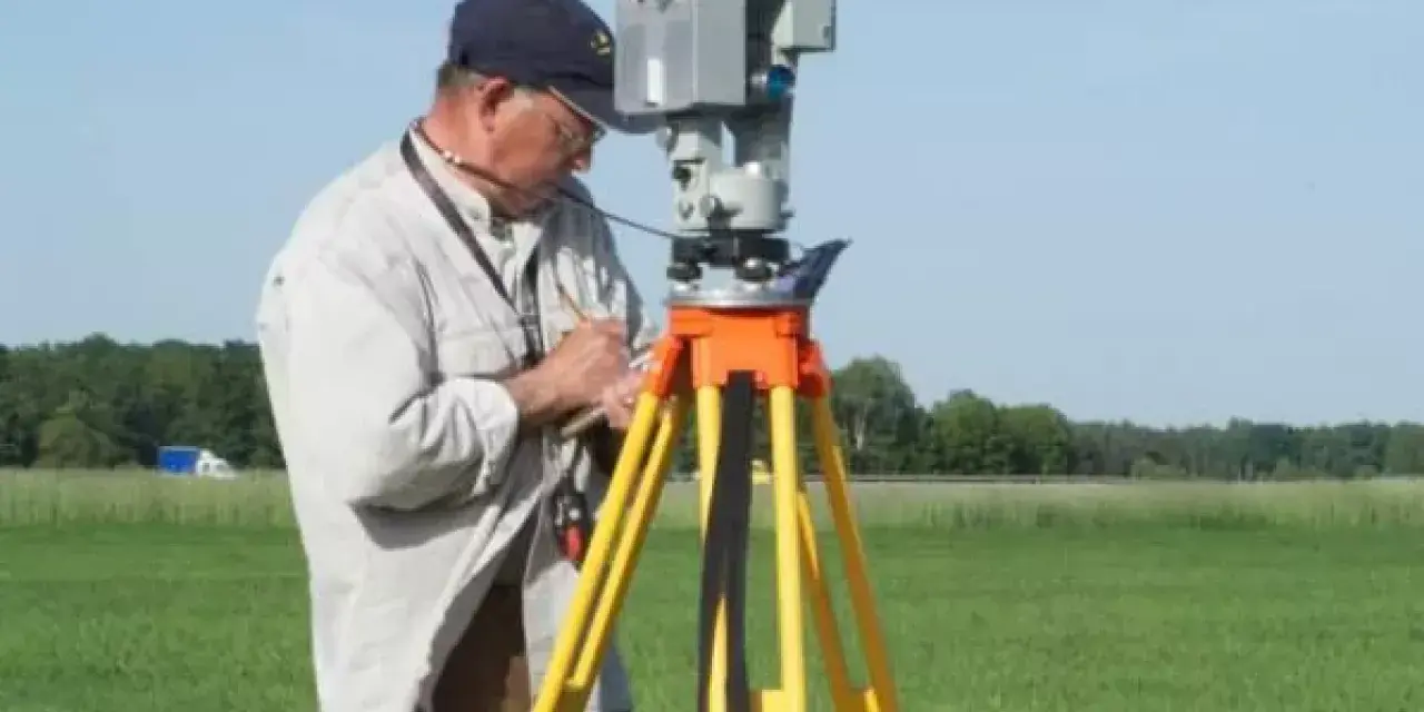 Geodeta precyzyjnie ustala granice działki, używając nowoczesnego sprzętu pomiarowego na tle zielonego pola.