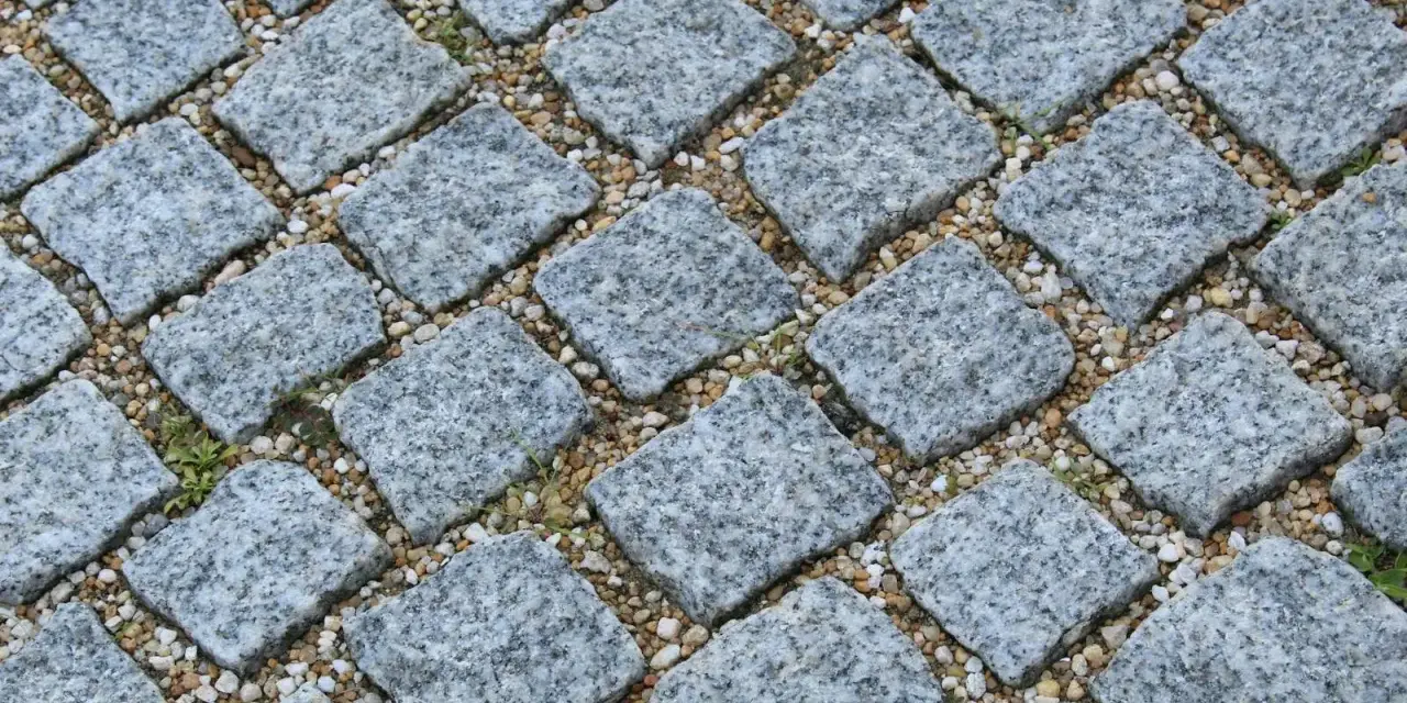 Szara kostka granitowa ułożona na podsypce. Widać, ile podsypki pod kostkę na m2 jest potrzebne do stabilnego ułożenia.