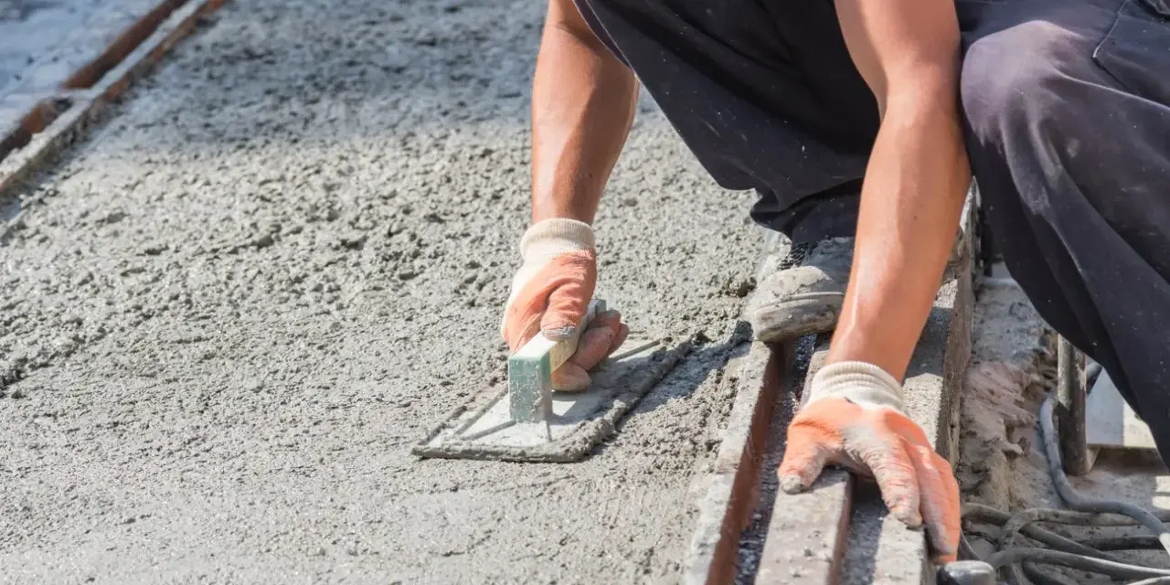 Pracownik w rękawicach wygładza świeży beton kielnią. To kluczowy etap, jak zrobić suchy beton, by był równy i trwały.