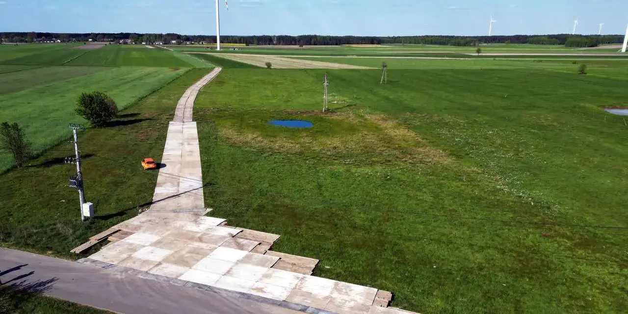 Teren budowy farmy wiatrowej z tymczasową drogą z płyt betonowych. Tłuczeń na drodze ułatwia dojazd ciężkiego sprzętu.