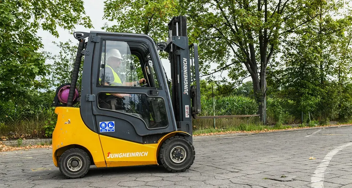 Operator w kasku i kamizelce prowadzi wózek widłowy Jungheinrich. Zastanawiasz się, ile kosztuje uprawnienia na wózek widłowy?