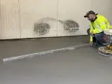 Pracownik w kamizelce odblaskowej wykonuje poziomowanie wylewki betonowej za pomocą łaty.