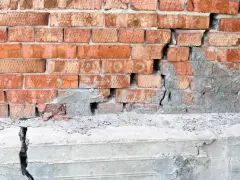 Uszkodzona ceglana ściana z pękniętym betonowym fundamentem. Podbijanie fundamentów cena – pilna naprawa.