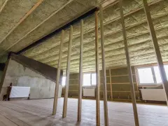 Ocieplenie stropu betonowego wełną mineralną. Widać drewnianą konstrukcję, okna i grzejniki.