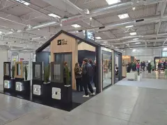 Stoisko targowe z oknami i drzwiami, z ekspozycją okien i ludźmi oglądającymi ofertę.