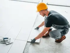 Fachowiec układa płytki na balkonie. Dowiedz się, ile kosztuje położenie płytek na balkonie i jakie materiały są potrzebne.
