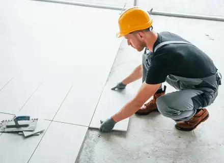 Fachowiec układa płytki na balkonie. Dowiedz się, ile kosztuje położenie płytek na balkonie i jakie materiały są potrzebne.