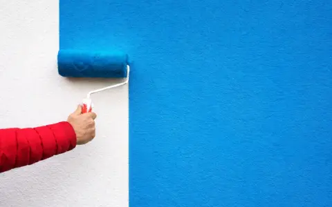 Malowanie ściany na niebiesko wałkiem. Ta farba wygłuszająca ściany nada pomieszczeniu nowy wygląd i poprawi akustykę.