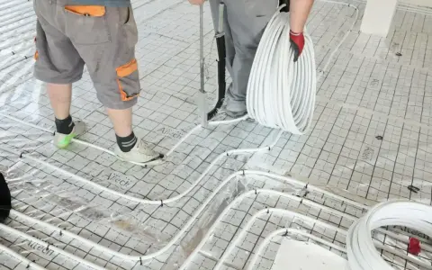 Pracownicy układają rury do ogrzewania podłogowego na siatce. Wkrótce powstanie tu szlichta, która zapewni komfort cieplny.