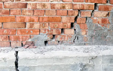 Uszkodzona ceglana ściana z pękniętym betonowym fundamentem. Podbijanie fundamentów cena – pilna naprawa.
