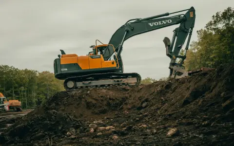 Pomarańczowo-czarna koparka Volvo EC220DL pracuje na budowie. Operator koparki gąsienicowej zarabia dobrze, wykonując ciężką pracę.